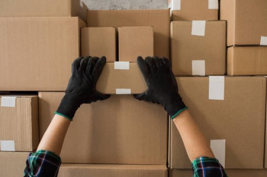 Cardboard boxes stocked by the wall in warehouse. Ready for delivery. Delivery person picking one of boxes.